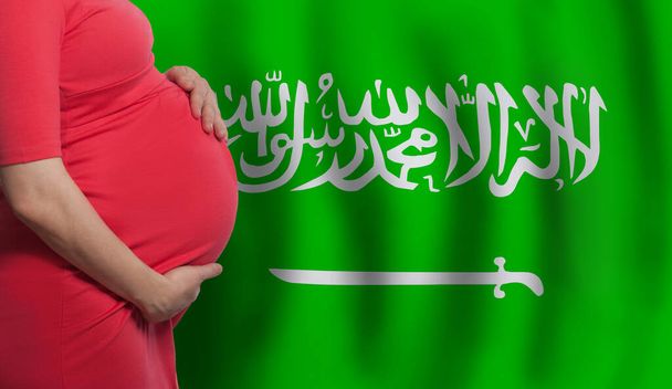 close-up zwangere vrouw buik op vlag van Saudi-Arabië achtergrond - Foto, afbeelding