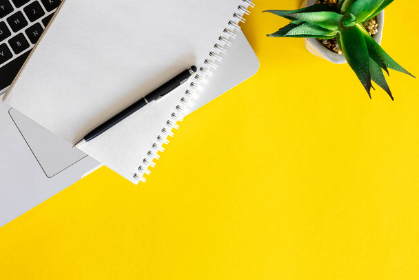 Ноутбук, блокнот і рослина на жовтому тлі, плоский. Мінімальний офісний фон, простір для копіювання. - Фото, зображення