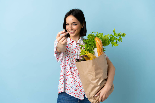 Mujer joven sosteniendo una bolsa de la compra de comestibles haciendo gesto de dinero - Foto, imagen