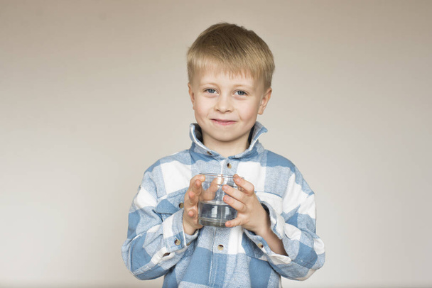 Niño bebe agua de un vaso sobre un fondo gris en el estudio - Foto, Imagen