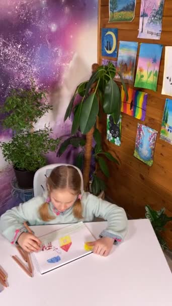 Genç sanatsal hayal gücü, çocukluk hobisi. Dikey sevimli küçük kız, sanatsal malzemeler, resimler ve kapalı alan bitkileriyle çevrili renkli kalemlerle yaratıcılığını neşeyle ifade ediyor. - Video, Çekim