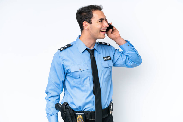 Young police caucasian man isolated on white background keeping a conversation with the mobile phone - Photo, Image
