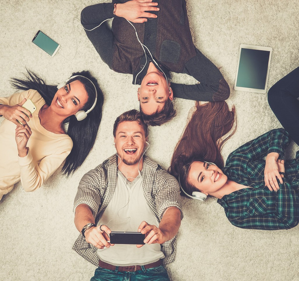 Heureux amis multiraciaux se détendre sur un tapis avec des gadgets
  - Photo, image