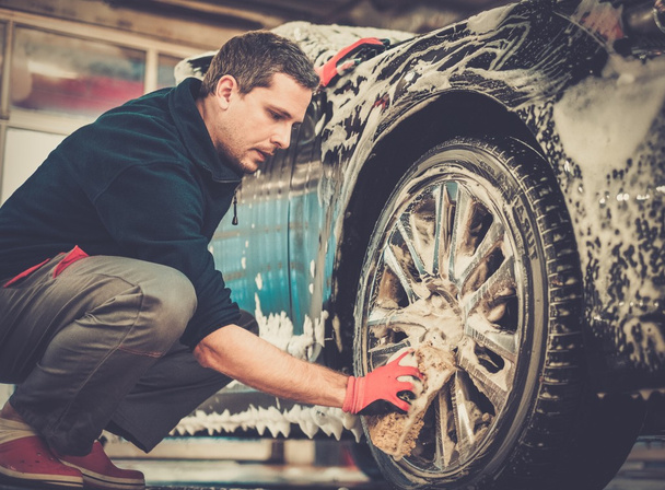 Hombre trabajador lavando ruedas de aleación de coche en un lavado de coches  - Foto, imagen