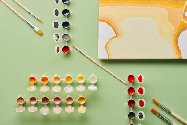 Pinsel und Acrylfarben und Leinwand zum Malen nach Zahlen. Grüner Hintergrund. Ansicht von oben. Flache Lage. - Foto, Bild