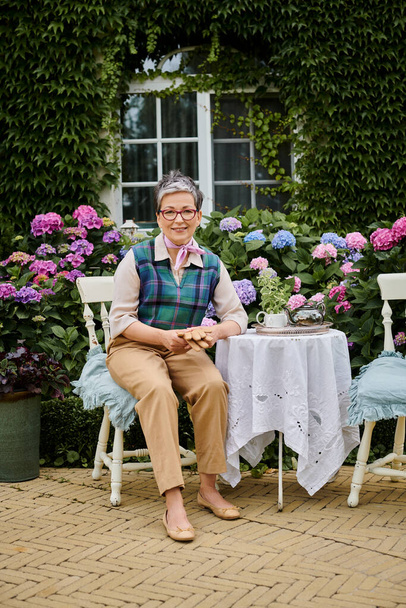 весела зріла жінка сидить в саду під час чаю біля будинку в Англії і дивиться на камеру - Фото, зображення