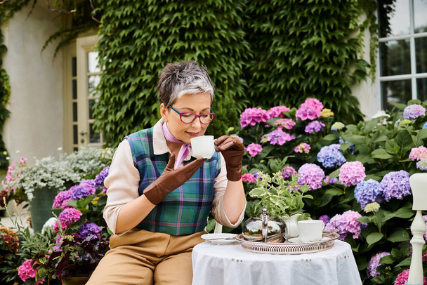 good looking jolly mature woman drinking hot tea at breakfast in garden of her house in England - Photo, Image