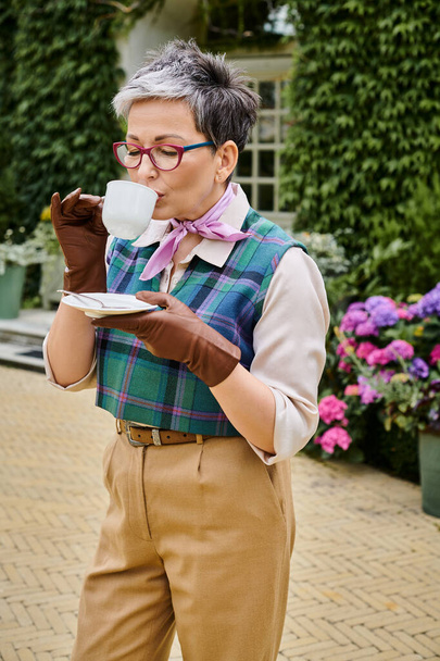 vonzó vidám érett nő iszik forró tea reggelinél kertjében háza Angliában - Fotó, kép