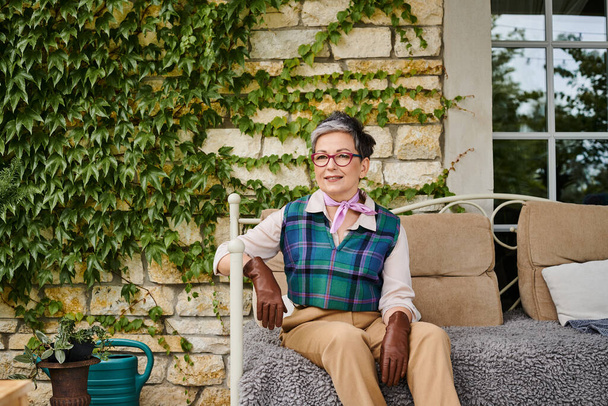 привлекательная веселая зрелая женщина сидит на диване возле своего дома в Англии и смотрит в камеру - Фото, изображение