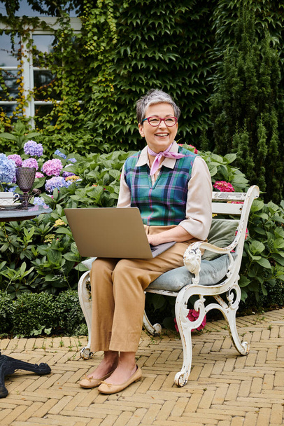 debonair érett vidám nő elegáns öltözékben ül laptop teaidőben közelében háza Angliában - Fotó, kép