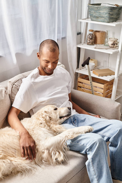 Человек с миастенией гравис расслабляется на диване со своей собакой-лабрадором, демонстрируя разнообразие и включение. - Фото, изображение