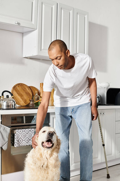 Un hombre afroamericano con miastenia gravis acaricia pacíficamente a su perro labrador en una acogedora cocina. - Foto, imagen