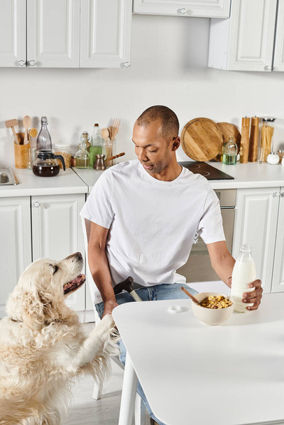 Niepełnosprawny Afroamerykanin siedzi przy kuchennym stole, ciesząc się towarzystwem swojego lojalnego psa labradora.. - Zdjęcie, obraz