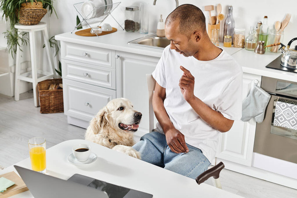 An African American man with a disability and his Labrador retriever enjoying a moment together in a cozy kitchen setting. - Фото, изображение