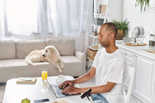 Postižený Afroameričan sedí u stolu s laptopem v doprovodu svého labradorského psa. - Fotografie, Obrázek