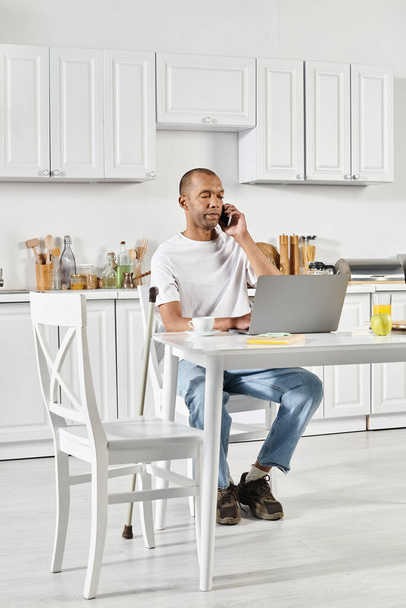 Um homem afro-americano deficiente com síndrome de Myastenia Gravis sentado em uma mesa de cozinha, profundamente envolvido em um telefonema. - Foto, Imagem