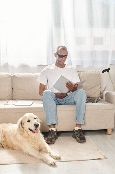 Ένας ανάπηρος Αφροαμερικανός με μυασθένεια gravis σύνδρομο κάθεται σε έναν καναπέ δίπλα σε ένα σκυλί Λαμπραντόρ, ενσωματώνοντας την ποικιλομορφία και την ένταξη. - Φωτογραφία, εικόνα