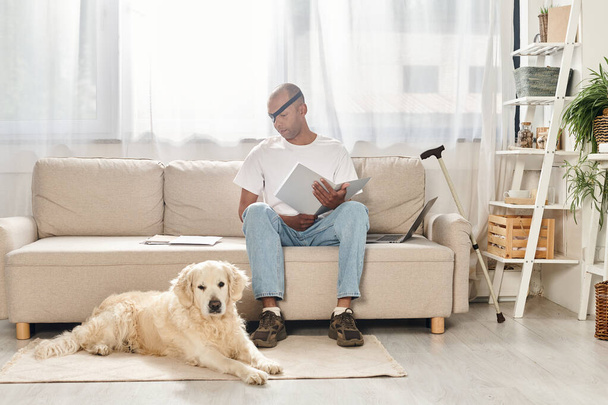 Een gehandicapte Afro-Amerikaanse man met myasthenia gravis syndroom ontspant op een bank naast zijn trouwe Labrador hond. - Foto, afbeelding
