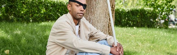 An African American man with myasthenia gravis syndrome sits beside a tree - Photo, Image