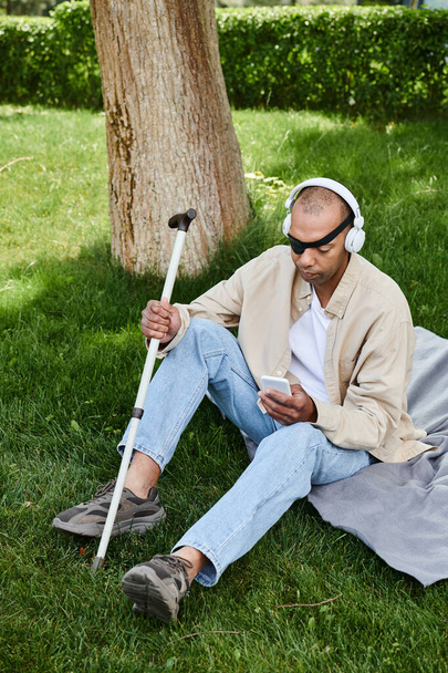 Egy afroamerikai férfi myasthenia gravis szindrómában ül a fűben, fejhallgatón keresztül zenét hallgat.. - Fotó, kép