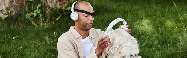 Un uomo afroamericano con la sindrome della miastenia grave si rilassa nell'erba con un cane Labrador che indossa le cuffie. - Foto, immagini