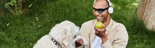 Різноманітний афроамериканський чоловік з міастенією гравієм тримає яблуко, а його собака Лабрадор стоїть поруч з ним. - Фото, зображення