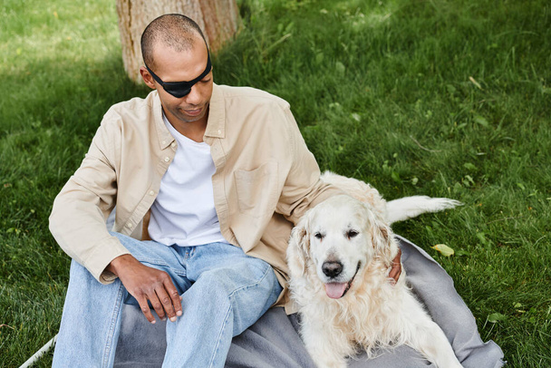 Інвалідний афроамериканський чоловік з міастенією гравієм сидить на ковдрі зі своїм вірним собакою Лабрадором, втілюючи різноманітність і включення. - Фото, зображення