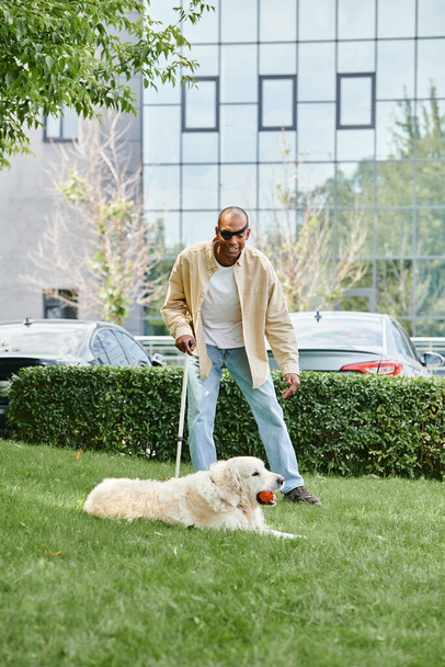 Ένας Αφρο-Αμερικανός με μυασθένεια Gravis περπατά πιστός Λαμπραντόρ σκυλί του σε ένα λουρί σε ένα καταπράσινο πεδίο. - Φωτογραφία, εικόνα
