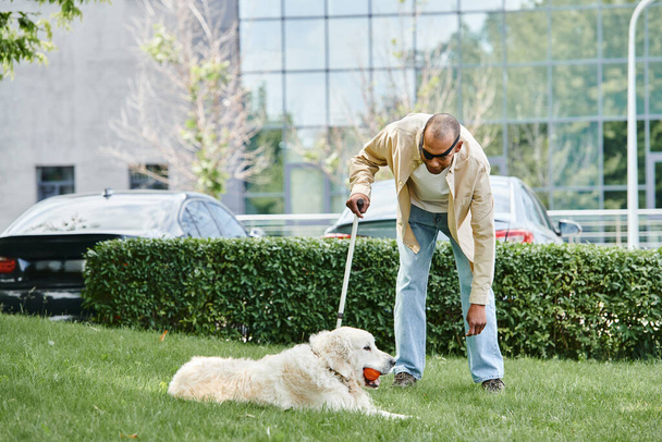 Vammainen afroamerikkalainen mies, jolla on myasthenia gravis, leikkii iloisesti Labrador-koiransa kanssa vehreässä ruohossa.. - Valokuva, kuva