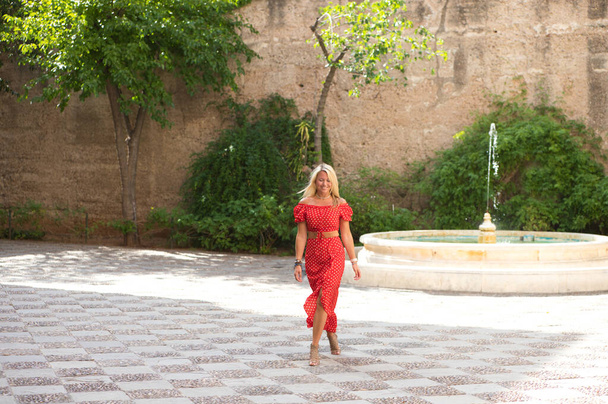 Mooie jonge blonde vrouw uit de Verenigde Staten is op een sightseeing trip in Sevilla, Spanje. Het meisje is gelukkig en bezoekt een plein met een marmeren fontein en mediterrane vegetatie.Travel concept - Foto, afbeelding