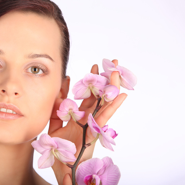 Sağlıklı cilt ve pembe orkide olan esmer kadın güzel yüzü - Fotoğraf, Görsel