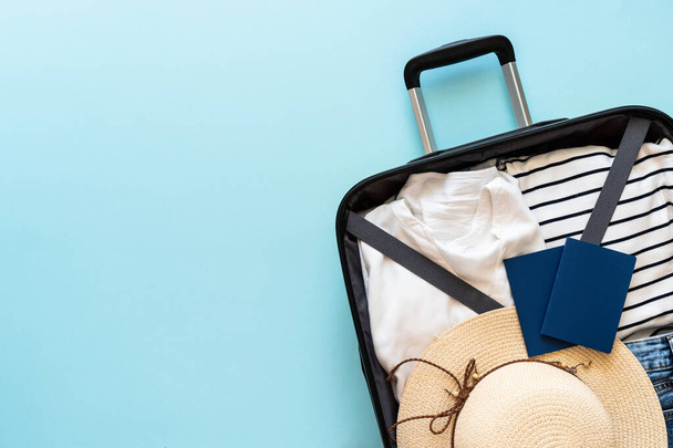 Ανοιχτή βαλίτσα με καλοκαιρινό ύφασμα, καπέλο και διαβατήριο σε μπλε φόντο. Επίπεδη εικόνα. - Φωτογραφία, εικόνα