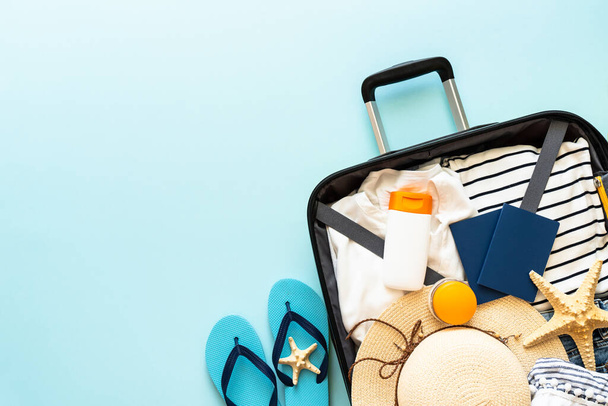 Ανοιχτή βαλίτσα με καλοκαιρινό ύφασμα, καπέλο και διαβατήριο σε μπλε φόντο. Επίπεδη εικόνα. - Φωτογραφία, εικόνα
