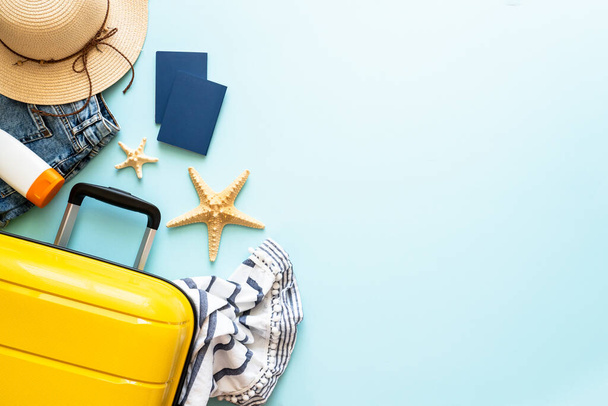 Travel background, summer holidays. Suitcase, passports, hat and summer cloth on blue background. Flat lay image with copy space. - Photo, Image