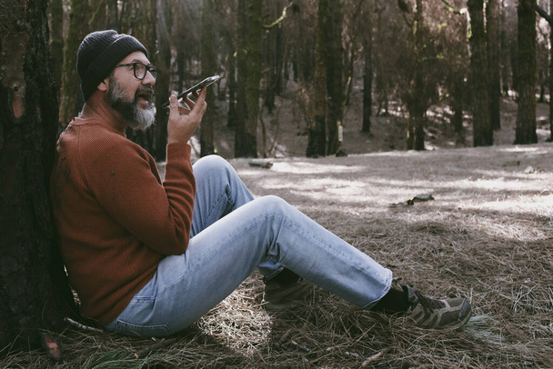 Jeden człowiek korzystający z telefonu w lesie, korzystający z technologii i rekreacji na świeżym powietrzu. Współczesny człowiek przemawiający w komórce z drzewami w tle. Ludzie i komunikacja w sprawie podróży - Zdjęcie, obraz