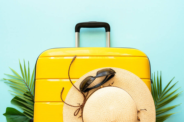 Summer holidays, traveling concept. Suitcase, hat and palm leaves on blue background. Flat lay with space for text. - Photo, Image