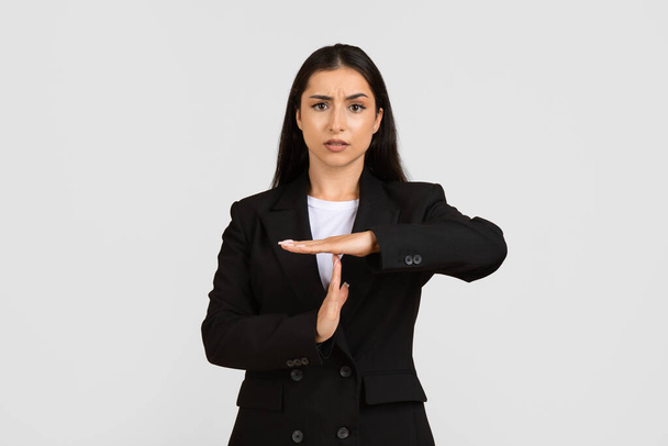 Zaostřená mladá evropská podnikatelka v černém obleku, s rukama na stopkách, s vážným výrazem, stojící na šedém pozadí - Fotografie, Obrázek
