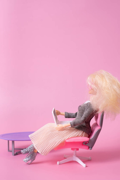 Muñeca con portátil en silla sobre fondo rosa. Trabajo en casa, concepto creativo freelance - Foto, imagen