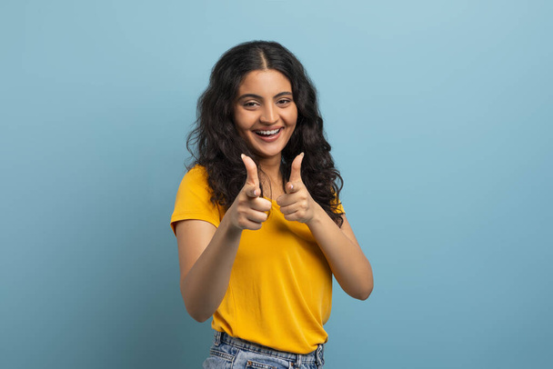 Positive junge indische Studentin zeigt mit beiden Händen in die Kamera und lächelt, posiert isoliert auf buntem blauem Studiohintergrund, Kopierraum. Gesten-Konzept - Foto, Bild