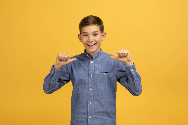 Веселый подросток, указывающий на себя пальцами с радостной улыбкой, счастливый мальчик в джинсовой рубашке, стоящий на ярко-желтом фоне, источающий уверенность и счастье, копирующий пространство - Фото, изображение