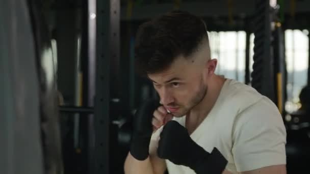 Közelkép Kaukázusi férfi bokszoló doboz képzés sötét tornaterem fitness klub izzadt motivált férfi sportoló bokszoló edzés ököl sztrájk ütések verés boxzsák profi sport edzés harc - Felvétel, videó
