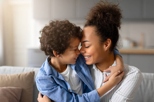 Rakastava musta äiti ja nuori poika koskettavat neniä rakastavassa hetkessä, lämpimät hymyt kasvoillaan, joilla on vahva äiti-lapsi-side. - Valokuva, kuva