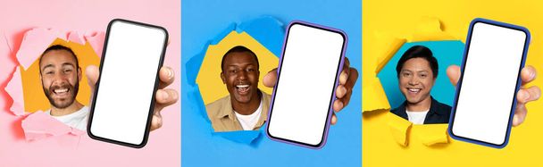Τρεις χαρούμενοι διεθνείς άνδρες από διαφορετικά εθνοτικά υπόβαθρα ξέσπασε μέσα από πολύχρωμο σχισμένο χαρτί, ο καθένας κρατώντας ένα smartphone με μια κενή οθόνη έτοιμη για προσαρμογή - Φωτογραφία, εικόνα