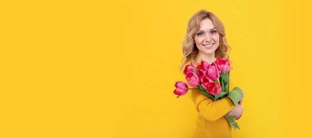 uśmiechnięta młoda kobieta z wiosennymi kwiatami tulipanów na żółtym tle. Kobieta odizolowany portret twarzy, baner z makietą przestrzeń kopiowania - Zdjęcie, obraz