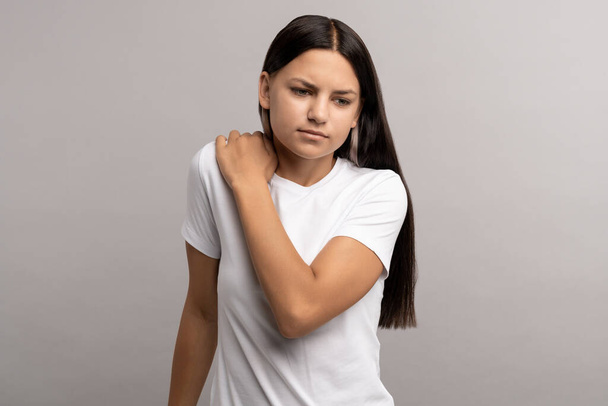 Αναστατωμένη έφηβος κορίτσι αισθάνονται δυσφορία πόνο μετά από μακρά μελέτη του υπολογιστή σε λανθασμένη στάση. Έφηβος με τσιμπημένο νεύρο στο οστό του λαιμού που προκύπτει από αιφνίδια κίνηση κατά τη διάρκεια σωματικής άσκησης, προπόνηση - Φωτογραφία, εικόνα