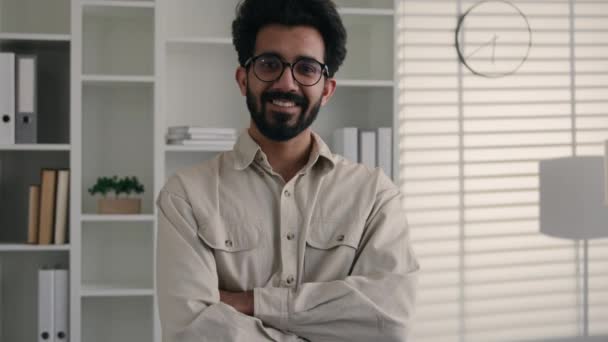 Männliches Porträt im Büro lächelnd glücklich zahmes Lächeln 30er Jahre bärtiger Geschäftsmann erwachsener Geschäftsmann professioneller Spezialist Chef Führer Unternehmer indische arabische muslimische Kerl Millennial gekreuzte Hände posieren - Filmmaterial, Video