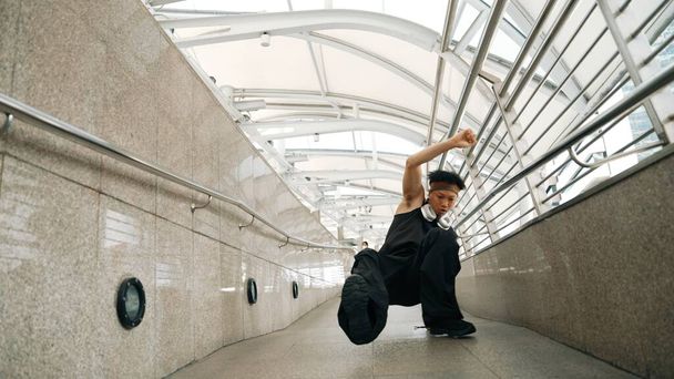 Στιγμιότυπο από έμπειρους χίπστερ που χορεύουν στο στενό διάδρομο. Επαγγελματική hip hop χορεύτρια δείχνουν b-boy βήμα στο διάδρομο, ενώ φορώντας κομψό ύφασμα. Υπαίθριο άθλημα 2024. Ελαφρώς. - Φωτογραφία, εικόνα