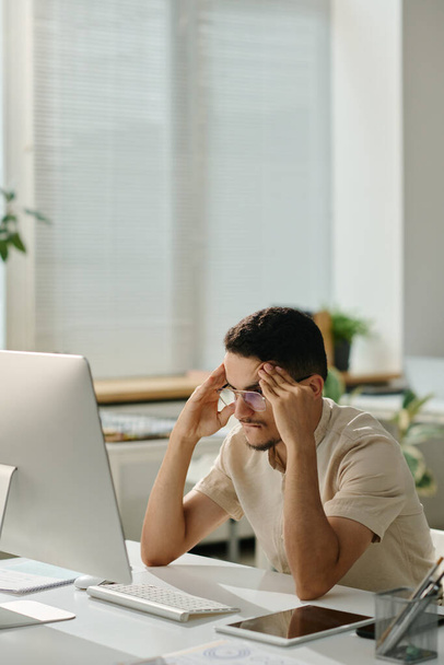 Angst mannelijke kantoormedewerker proberen te concentreren terwijl zitten in de voorkant van het computerscherm en kijken naar uploaden pagina - Foto, afbeelding