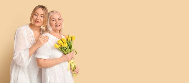 テキストのためのスペースを持つベージュの背景に花と彼女の大人の娘の花束を持つ女性. 母の日のためのバナー - 写真・画像