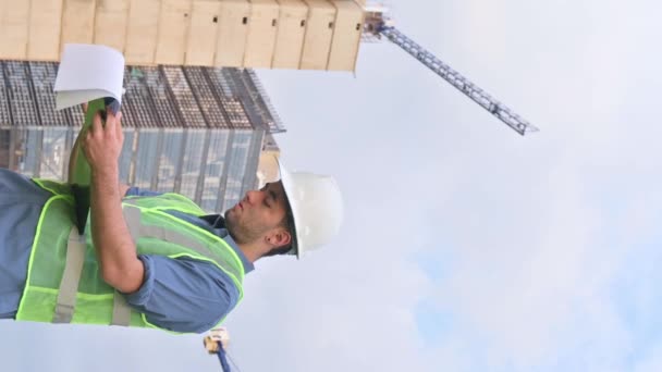 Güneşli bir günde inşaat alanında belge arayan Latin inşaat işçisinin dikey videosu. - Video, Çekim